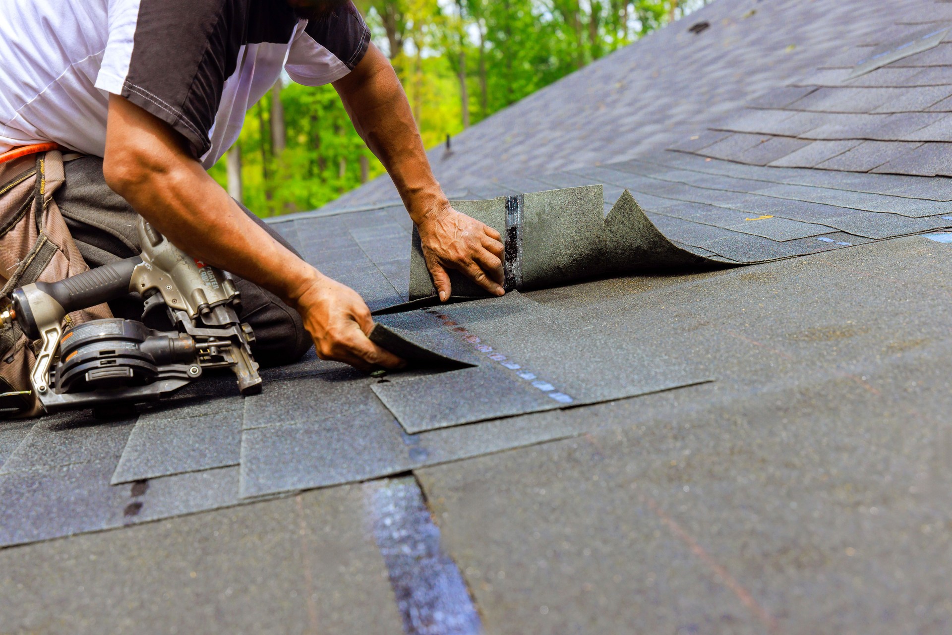 Construction worker using pneumatic nail gun to install new bitumen shingles on a roof